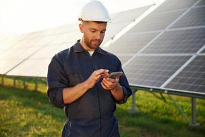 Phone, in hands, internet connection. Man is working with solar panels outdoors at daytime photo