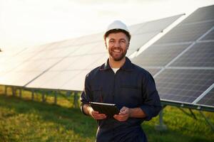 Digital,, tablet in hands. Man is working with solar panels outdoors at daytime photo