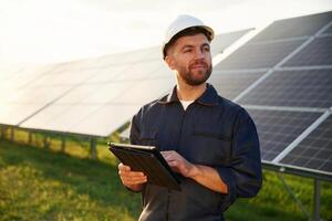 Digital ,tablet in hands. Man is working with solar panels outdoors at daytime photo