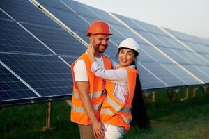 Playful mood,, embracing each other. Man and woman, workers are near solar panels, in uniform photo