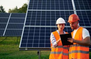 Man and ,woman, workers are near solar panels, in uniform photo