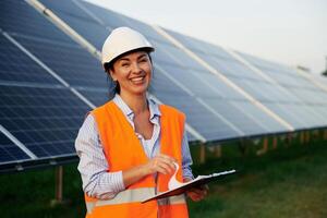 Checking the,, data, with notepad. Female worker engineer in uniform is near solar panels photo