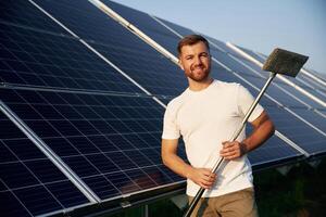 Mop, in hands. Man is working with solar panels outdoors at daytime photo