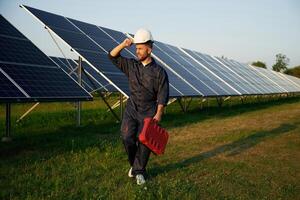 Red, case in hand. Man is working with solar panels outdoors at daytime photo