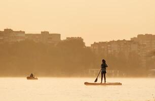Illuminated by ,,,sunlight. ...Girl kid is on the sup board, on the lake photo