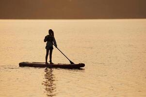 Girl kid is on the sup board during sunset, on the lake photo