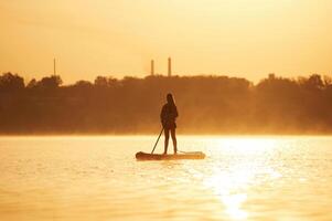 Illuminated by sunlight. Girl kid is on the ,,sup board, on the lake photo