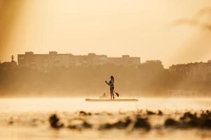 Illuminated ,,by, sunlight. Girl kid is on the sup board, on the lake photo