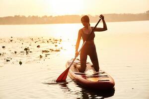 One ,person against sunlight. Young ,woman is with the sup board on the lake photo