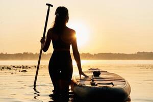 Enjoying the sunset, illuminated... Young woman is with the sup board on the lake photo