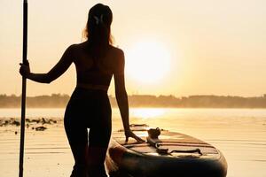 Enjoying ,,the ,sunset, illuminated. Young, woman is with the sup board on the lake photo