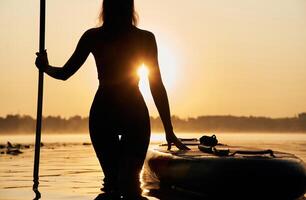Black silhouette,, sunset, illuminated. Young woman is with the sup board on the lake photo
