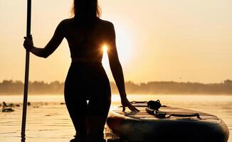 Black silhouette, sunset, illuminated. Young ,woman is with the sup board on the lake photo