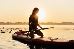 Darkened,, illuminated, by sunlight. Young woman is with the sup board on the lake photo