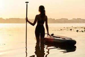 Enjoying,,, the sunset, illuminated. Young woman is with the sup board on the lake photo