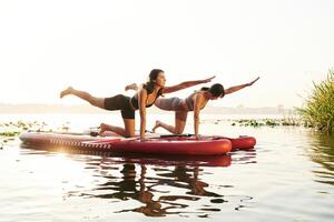 Doing yoga exercises, asana. Women, friends are on sup board on the lake together photo