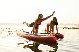 Doing yoga ,,exercises, asana. Women friends are on sup board on the lake together photo