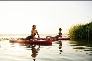 Asana,, doing yoga exercises. Women friends are on sup board on the lake together photo