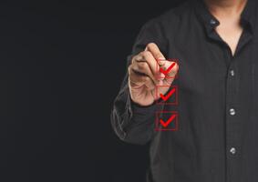 Businessman holding a pen and checking a mark on the boxes symbol is one of three options while standing on a black background. photo
