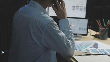 A man is sitting at a desk with a computer and a phone video