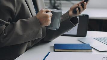 A person in a suit holding a coffee mug and using a cell phone video
