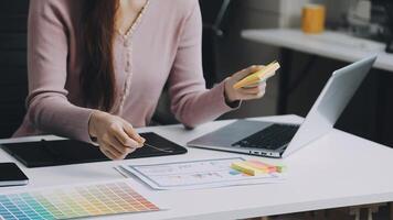A woman is sitting at a desk with a laptop and a color palette video