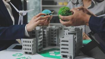 A group of people are holding a model of a building with a green plant video