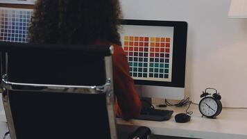 A woman sitting at a desk with a computer and a color palette video