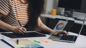A woman is working on her laptop with a pen and a color palette video