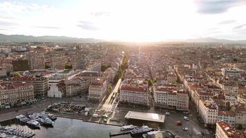 Aerial view of Marseille, France at golden hour, looking up from the Old Port into the city center. Sunlight streams over rooftops, casting long shadows and illuminating the urban layout. video