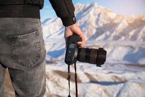 A person holding a camera in front of a mountain photo