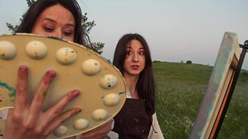Two girlfriends enjoy spending time together painting landscapes in nature. They communicate with each other, smile and enjoy the process of learning. video