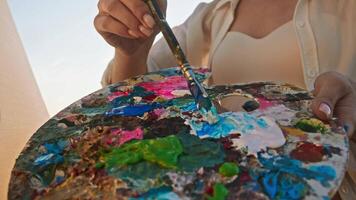 The artist mixed blue paint with white to create a light blue color and then started painting the sky in the natural scene. Close up. video