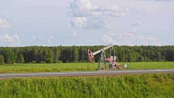 There is an oil rig located on side of a road in field, pumping oil. Due to its proximity to highway, it is convenient for transporting oil. wide shot video