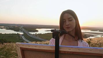 Budding artist delights in creating masterpiece on canvas with acrylic paints, taking in final moments of summer sun's rays on breathtaking scene. video