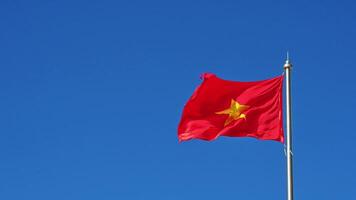 red Vietnamese flag with a yellow star on a high flagpole flutters in the wind on the background of blue sky video