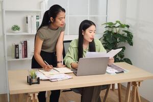 Portrait of Asian woman is standing writing in a notebook while discussing ideas with a colleague sit in front of a laptop. photo