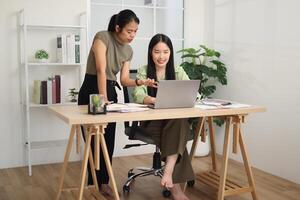 Two female employees are working together at a desk, discussing documents while looking at a laptop screen. Business ideas and strategies photo