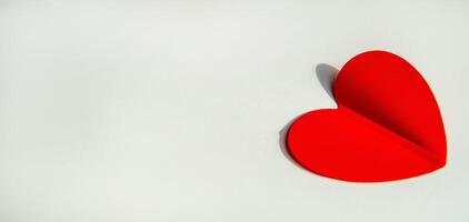 Banner with paper decoration in the shape of a red heart on a white background. Flat plan, top view, space for text on the left side photo