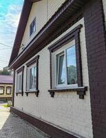 Side view of a one-story brick house with three plastic windows and a gable covered with modern siding photo