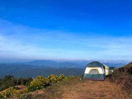 Row of tents located on the top of the hill with the panorama view of mountain and clear blue sky in background photo
