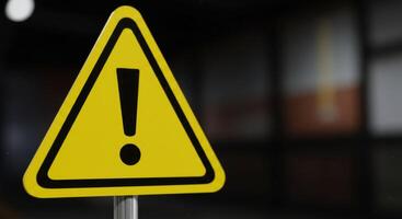 CloseUp of a Yellow and Black Warning Sign with Exclamation Point Against Dark Background photo