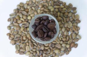 Roasted coffee beans in a glass with unroasted coffee beans in the background photo
