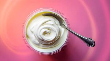 Delicious yogurt in plastic cup with spoon on pink background, top view. Space for text photo