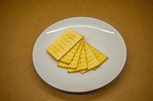 A stack of crisp, rectangular crackers on a white plate, set against a warm brown background. Ideal for snack, food, or appetizer themes photo