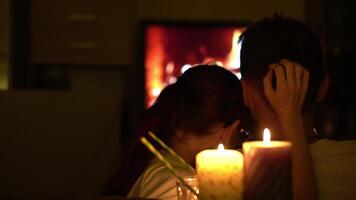 couple sits close together, their silhouettes illuminated by warm glow of candles and a cozy fireplace video