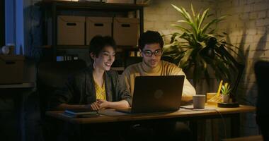 Young handsome man showing young woman to a colleague something on the laptop screen and explaining. They both laugh happily while looking at the screen while sitting at the desk in the office. photo