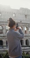 A young beautiful lady taking photos of the sights of Rome on a mobile phone, standing on an observation deck near the Coliseum. in 4k, red komodo, vertical
