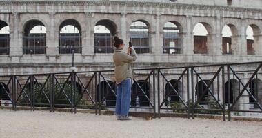 Warmly dressed woman of European appearance takes photographs of the sights of Rome on a mobile phone, standing on an observation deck near the Coliseum. in 4k, red komodo. photo