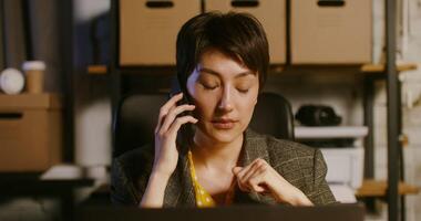 Woman of European appearance talking on a mobile with a serious look, sitting in front of an open laptop at a table in a modern stylish office photo